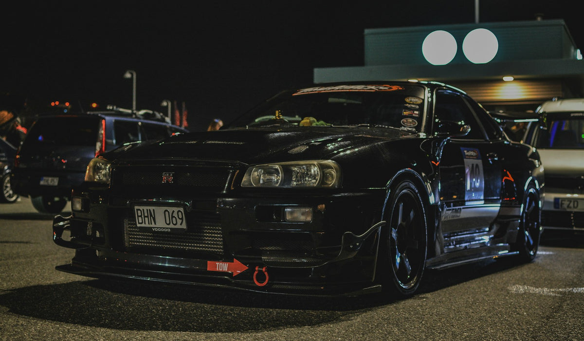 Modified black Japanese sports car parked at night before a car meet
