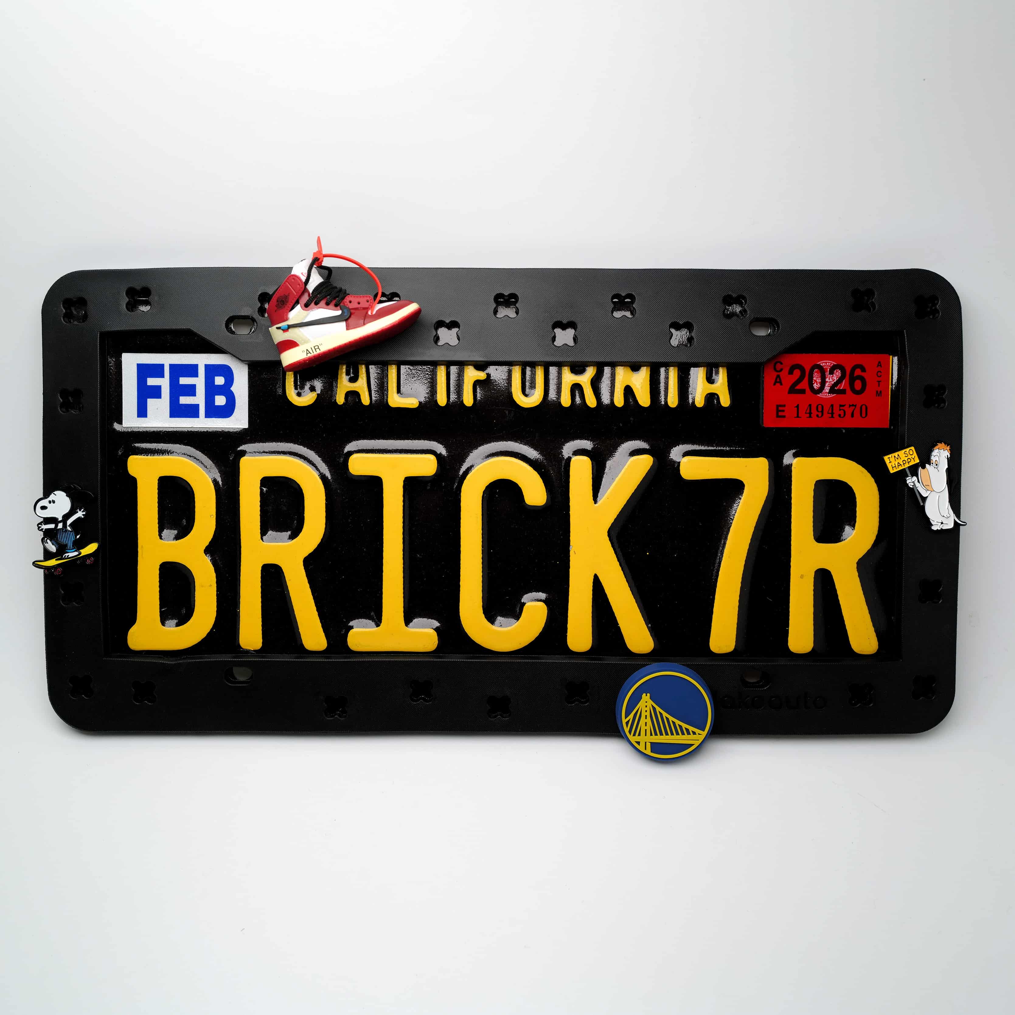 A sleek black Makoauto DIY license plate frame decorated with premium streetwear and sports theme charms, beautifully installed on a car rear