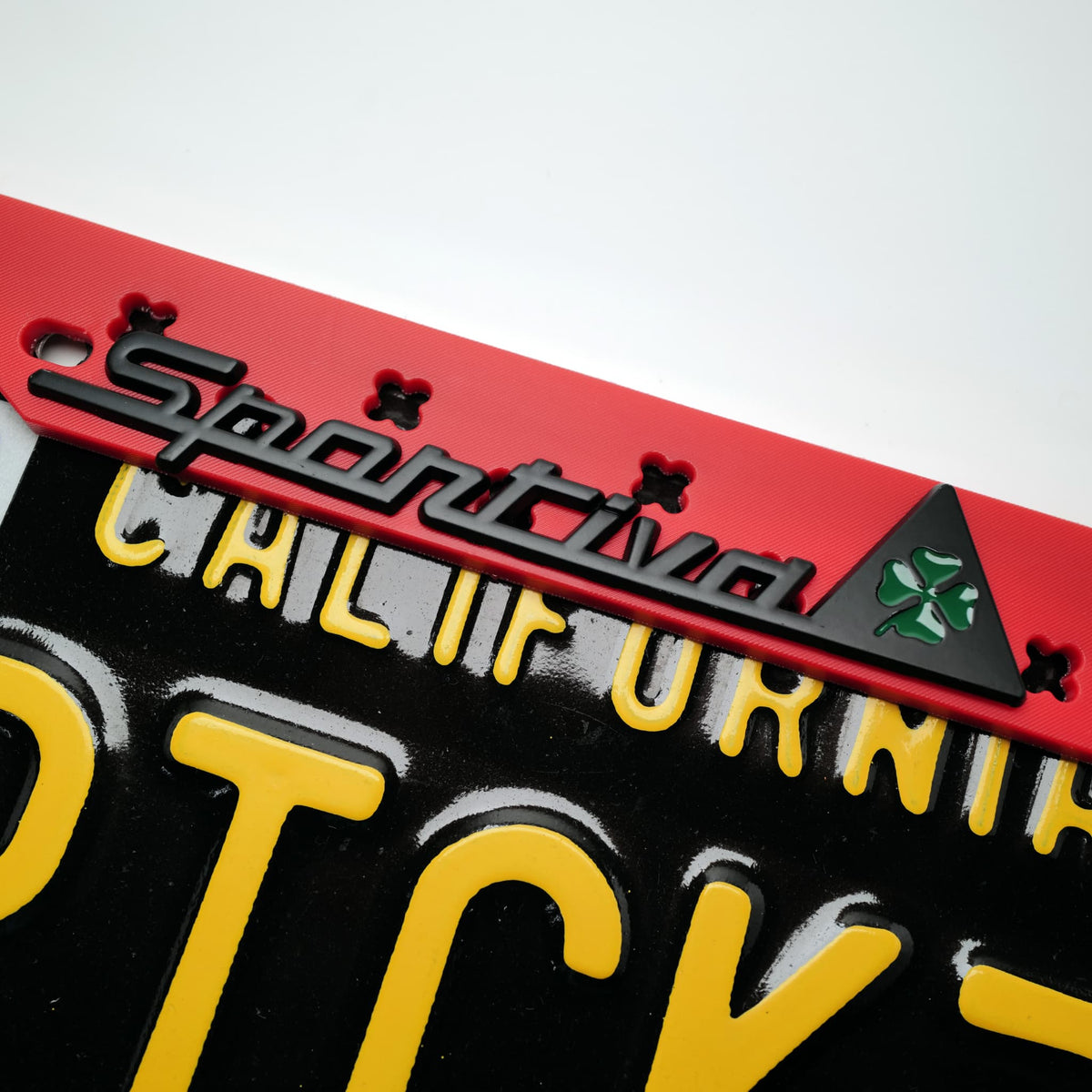 Detail view of the classic "Sportiva" script detail at the top center of the matte red license plate frame.