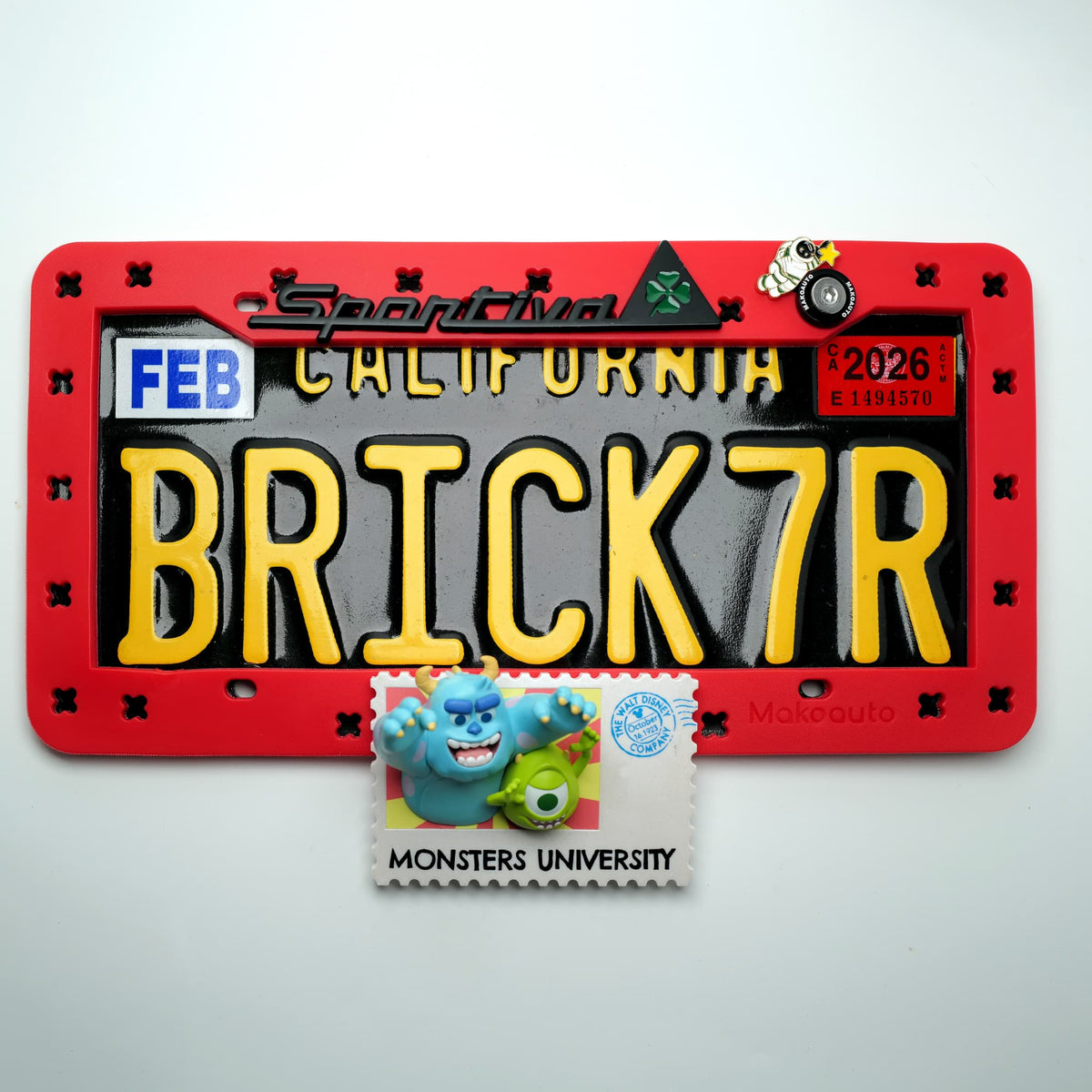 Close-up detail of the heavy-duty metal car logo emblem charm snapped into the red Makoauto TPU license plate frame